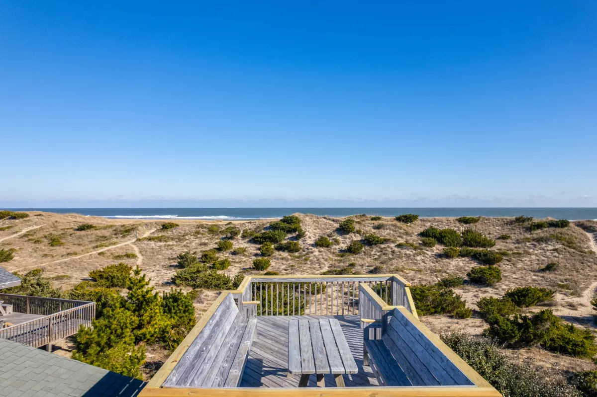 A wooden deck with a view of the ocean and dune landscape, furnished for comfort and offering space for lounging or dining. The setting suggests relaxation, alfresco meals, or social gatherings with a stunning Atlantic backdrop.