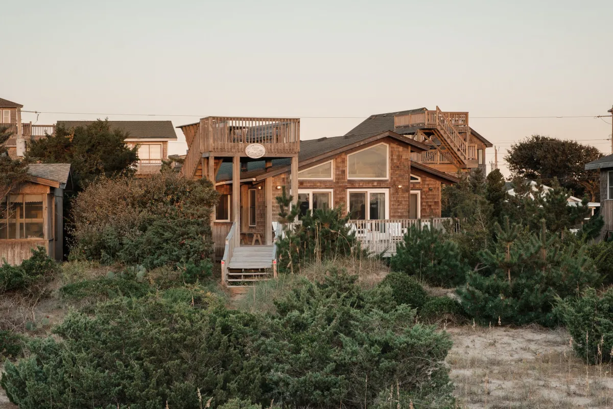 A broad wooden deck overlooks a lush yard, surrounded by greenery and large windows. The space invites gatherings, outdoor meals, or yard games, suggesting a welcoming setting for friends, family, and pets.