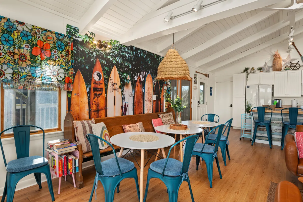 A playful and vibrant dining area with a central dining table, surfboard wall art, and a floral window treatment. The setting exudes a casual, coastal vibe, ideal for family meals and lively gatherings.