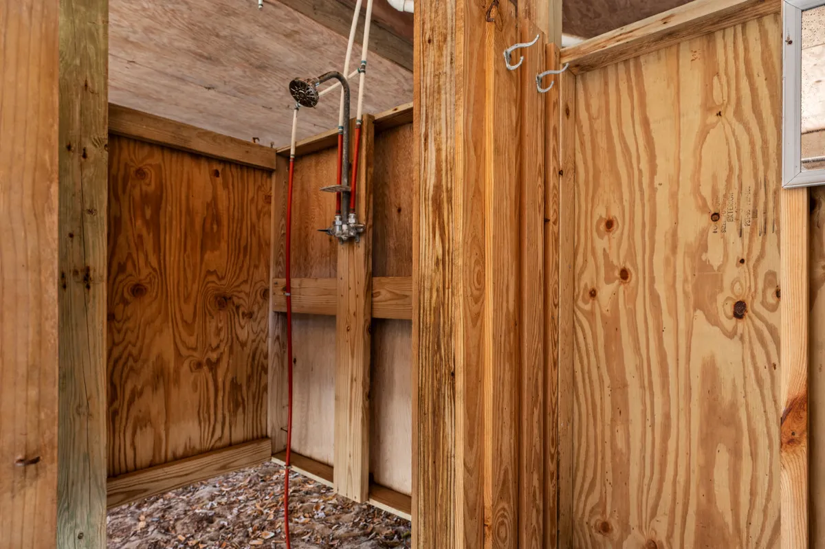 A rustic outdoor shower with wooden walls and modern fixtures, open to nature and designed for rinsing off after beach activities. The setting exudes a refreshing and liberating outdoor experience.