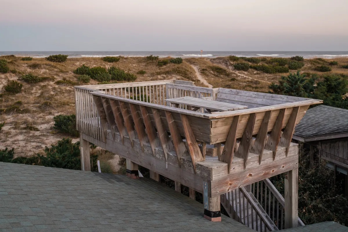 A wooden rooftop deck overlooking sweeping ocean views and a dune landscape. The deck is ideal for relaxing, socializing, or unwinding after a day by the water, capturing both the excitement of the outdoors and the comfort of home.