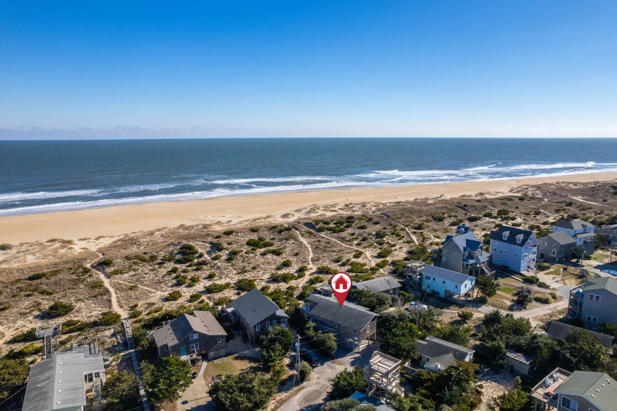 A wide beach scene features gentle waves rolling onto the sand, with nearby houses and a path leading to the ocean. The atmosphere is calm and inviting, ideal for beachcombing or savoring local seafood at nearby venues.