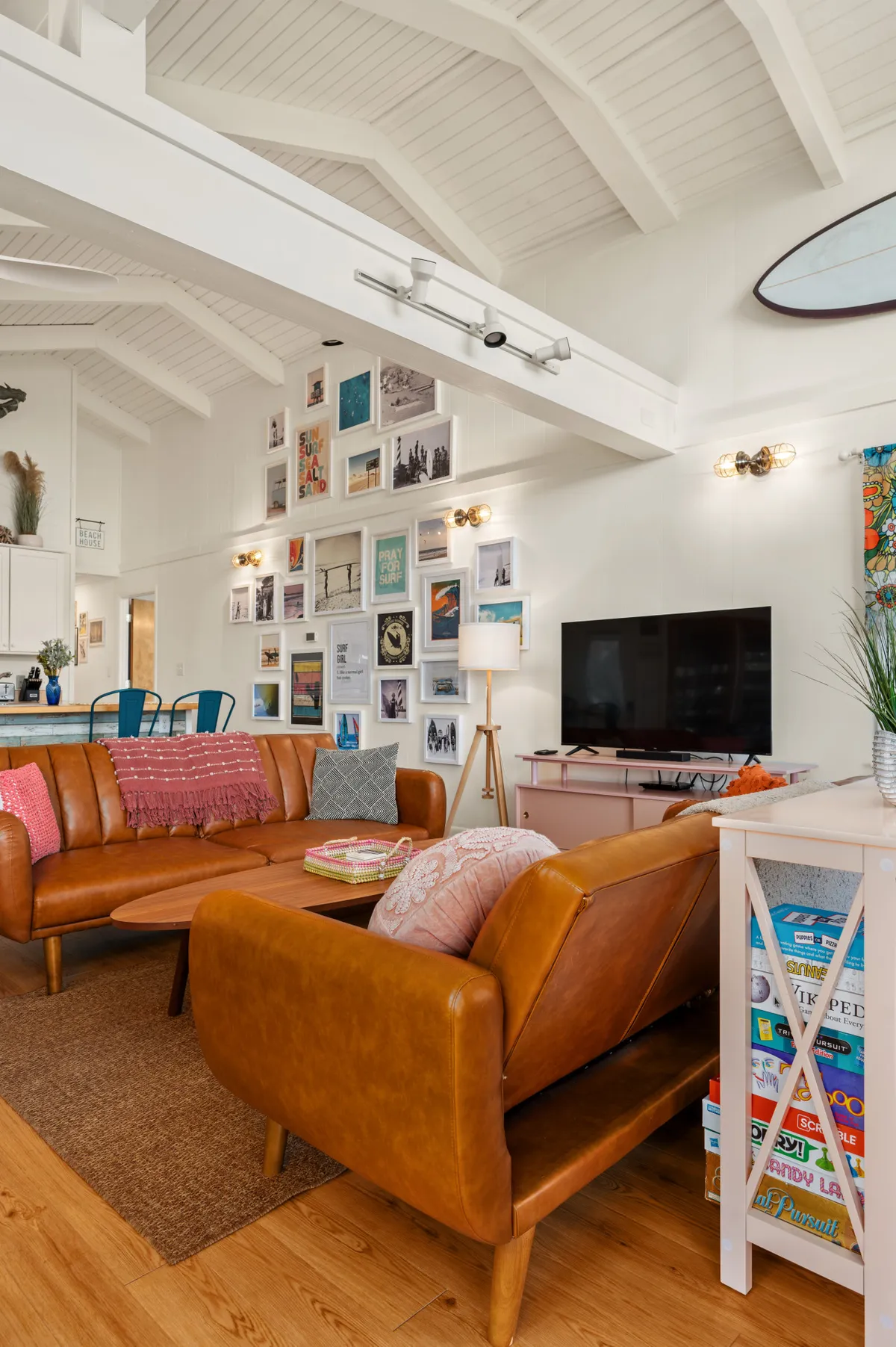 A warm, cozy living area with leather sofas, a central coffee table perfect for board games or puzzles, a gallery wall, a television, and decorative plants. The room feels both inviting and functional, ideal for relaxing evenings or lively game nights.
